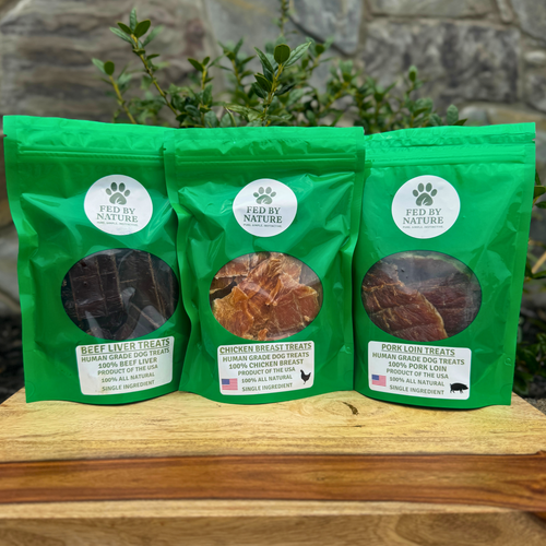 Three green packages of 'Fed by Nature' dog treats on a wooden surface with a natural background.