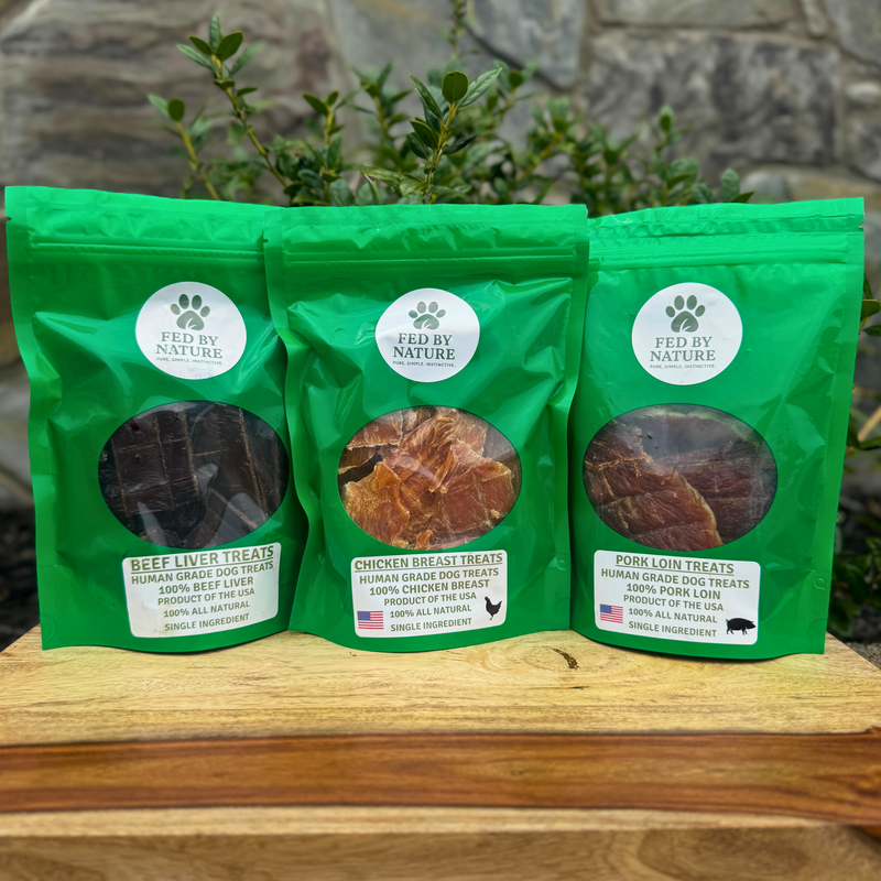 Three green packages of 'Fed by Nature' dog treats on a wooden surface with a natural background.